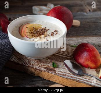 Hausgemachter Joghurt, gemischt mit frischen roten Äpfeln, serviert mit Leinsamen in einer Schüssel auf einem Holztisch. Gesundes glutenfreies und kohlenhydratartiges Frühstück oder Snack Stockfoto