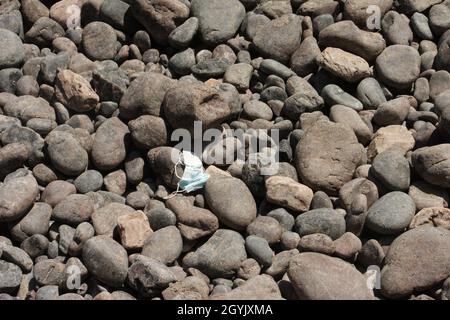 Weggeworfene Gesichtsmaske am Kieselstrand Stockfoto