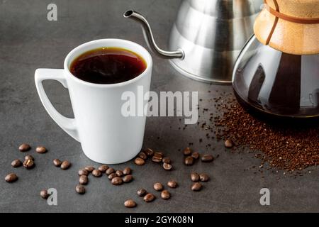 Eine Tasse Kaffee und die dritte Generation gießen über die Kaffeemaschine auf dem Steinboden Stockfoto