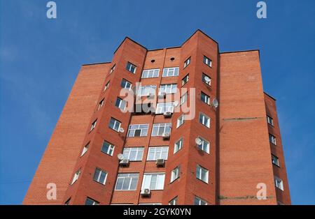 Mehrstöckige Backsteinfassade aus Hausrot gegen den blauen Himmel. Stockfoto