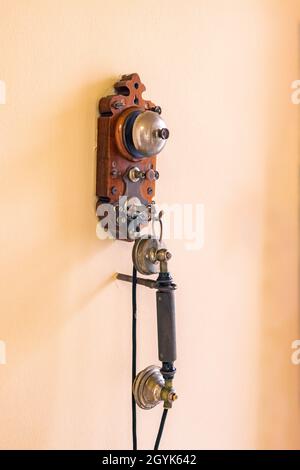 An einer gelben Wand hängt ein altes schnurgebundenes Telefon. Eines der ersten Telefone in Europa aus den 1880er Jahren Stockfoto