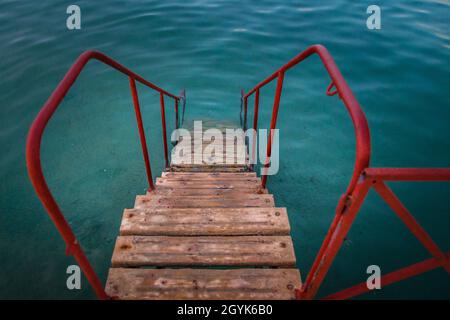 Hoch anwinklige Aufnahme einer hölzernen Treppe mit roten Geländern, die zum Wasser führen Stockfoto