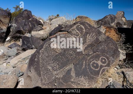 Anthropomorphe Figuren, die auf einem Basaltsteinblock in der Petroglyph-Stätte Three-Flues, New Mexico, geschnitzt wurden. Stockfoto