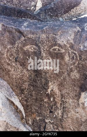 Ein menschliches Gesicht, das auf einem Basaltsteinbrocken in der Petroglyph-Stätte Three-Flues, New Mexico, geschnitzt wurde. Stockfoto