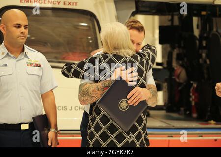 Petty Officer 3rd Class James Chandler und Frau Julia Weisinger umarmen sich bei einer Zeremonie, die zu Ehren von Chandlers Aktionen während des tropischen Sturms Imelda in der Air Station Houston, 15. Januar 2020, stattfand. Chandler sorgte für mehr als eine Stunde lang für lebensrettende Versorgung von Weisinger und sorgte dafür, dass sie sich stabilisieren und eine vollständige Genesung vornehmen konnte. (USA Foto der Küstenwache von Paige Hause der 3. Klasse) Stockfoto