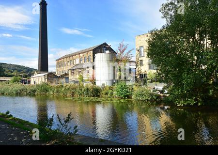 Verkommene Fabrik und großer Kamin auf dem Leeds - Liverpool Kanal in Bingley, West Yorkshire Stockfoto