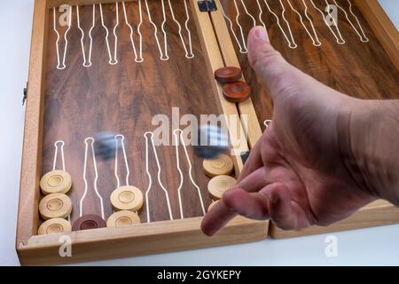 Bewegliche Würfel hängen in der Luft. Die Hand wirft die Würfel auf den Hintergrund von Brettspielen (Backgammon). Stockfoto