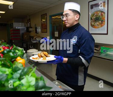 200118-N-ZI768-1032 NEWPORT NEWS, VA. (Jan 18, 2020) kulinarische Spezialistin Seaman Lehrling Isaac Rodriguez, der dem allgemeinen Chaos an Bord des Flugzeugträgers USS George Washington (CVN 73) der Nimitz-Klasse zugeteilt wurde, serviert Essen in der Kombüse an Bord der schwimmenden Unterkunft. George Washington wird derzeit in der Newport News Shipyard einer Überholung des Tankkomplexes (RCOH) unterzogen. Bei RCOH handelt es sich um ein fast vierjähriges Projekt, das nur einmal während der 50-jährigen Lebensdauer eines Trägers durchgeführt wird. Dazu gehören die Betankung der beiden Kernreaktoren des Schiffes sowie umfangreiche Reparaturen, Upgrades und Modernisierungen. (USA Navy ph Stockfoto