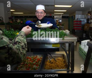 200118-N-ZI768-1025 NEWPORT NEWS, VA. (Jan 18, 2020) kulinarische Spezialistin Seaman Lehrling Isaac Rodriguez, Zentrum, der dem allgemeinen Chaos an Bord des Flugzeugträgers USS George Washington (CVN 73) der Nimitz-Klasse zugewiesen wurde, serviert Nahrung für die Luftbesatzung Survival Equipmentman Airman Lehrling Brianna Burgess, der an die Zwischeninstandhaltungsabteilung des Flugzeugs an Bord von George Washington, In der Kombüse an Bord der schwimmenden Unterkunft. George Washington wird derzeit in der Newport News Shipyard einer Überholung des Tankkomplexes (RCOH) unterzogen. RCOH ist ein fast vierjähriges Projekt, das nur einmal während eines Autos durchgeführt wird Stockfoto