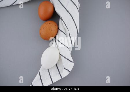 Gesprenkelte, braune und weiße Eier liegen flach organisches Styling auf zerknittertem Geschirrtuch, Serviettenstruktur abstrakter Hintergrund. Draufsicht, mittlere Komposition. Stockfoto