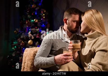 Mann und Frau trinken Kakao auf der Couch neben dem geschmückten Neujahrsbaum zu Hause. Stockfoto