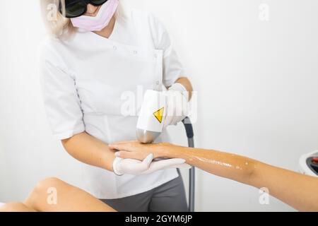 Der Epiliermeister entfernt Haare mit einem Laser aus der Hand des Patienten Stockfoto