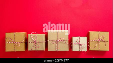 Geschenkschachteln mit weihnachtlich rot weiß gestreiften Band Schleife, braunes Kraftpapier Weihnachtsgeschenke auf rotem Hintergrund, Draufsicht. Selbstgemachte diy Eco wr Stockfoto