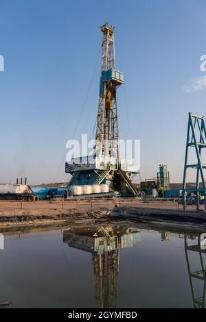 Ein Ölbohrgerät spiegelt sich im Wasser der Reservegrube auf einem Bohrplatz in der Green River Desert von Utah wider. Stockfoto