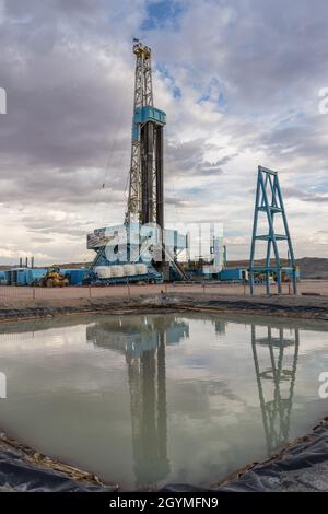 Ein Ölbohrgerät spiegelt sich im Wasser der Reservegrube auf einem Bohrplatz in der Green River Desert von Utah wider. Stockfoto