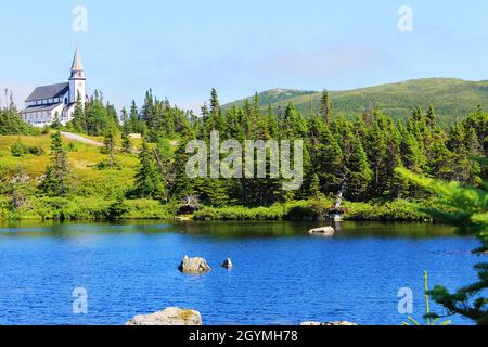 Blick über einen Teich zu einer Kirche auf einem Hügel, umgeben von Wald. Stockfoto