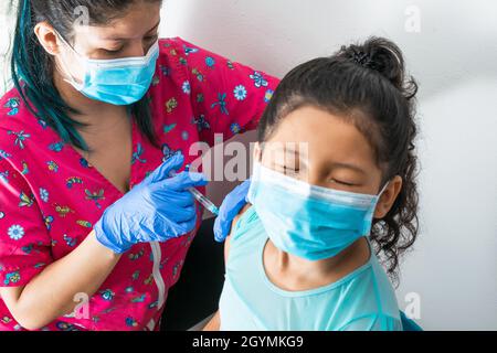 Kinderkrankenschwester injiziert braunen Mädchenarm. Arzt injiziert covid-19-Impfstoff. Mädchen schließt ihre Augen vor starken Schmerzen und schaut weg, Grippeschutzimpfung. medica Stockfoto