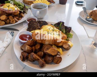 Blick von oben auf ein großes Frühstücksangebot mit Eiern benedict, fingelnden Kartoffeln und putenwurst-Patties auf einem Marmortisch in einem Lokal Stockfoto