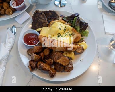 Blick von oben auf ein großes Frühstücksangebot mit Eiern benedict, fingelnden Kartoffeln und putenwurst-Patties auf einem Marmortisch in einem Lokal Stockfoto