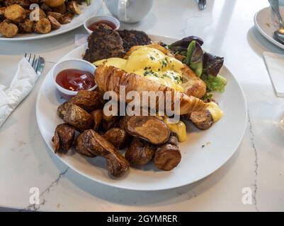 Blick von oben auf ein großes Frühstücksangebot mit Eiern benedict, fingelnden Kartoffeln und putenwurst-Patties auf einem Marmortisch in einem Lokal Stockfoto