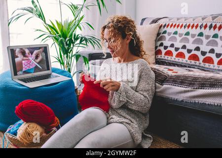 Gemütliche Strickfrau folgen Tutorial in gestrickten Winter warmen Pullover und im Pyjama genießt stricken Arbeit auf rot karierten karierten karierten Decke zu Hause in gemütlichen Wint Stockfoto