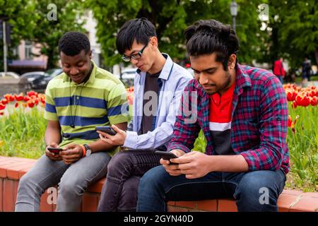 Junge Männer verschwenden Zeit mit Gadgets während der Sitzung im Park Stockfoto