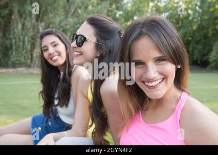 Closuep-Aufnahme von drei Frauen mit unterschiedlichen Ethnien im Park, die sitzen und ein Selfie machen Stockfoto