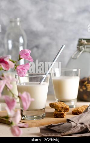 Zwei Gläser und eine Flasche Milch, Müsliriegel, einige Nüsse und Rosinen in einem Glas und eine braune Serviette mit rosa Blüten. Stockfoto
