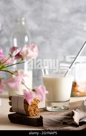 Zwei Gläser und eine Flasche Milch, Müsliriegel, einige Nüsse im Glas und eine braune Serviette mit rosa Blüten. Stockfoto