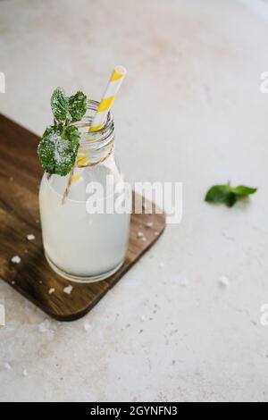 Erfrischendes Limonadengetränk im Sommer in einer Glasflasche, die mit gelbem Papierstroh und Minze dekoriert ist Stockfoto
