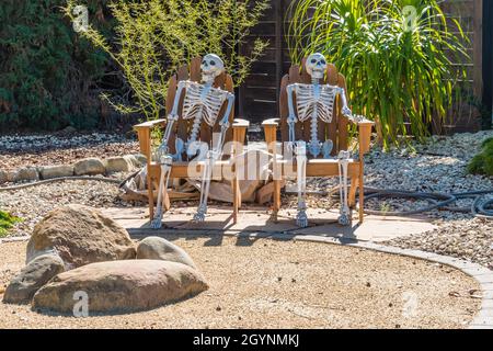 Zwei halloween-Skelette sitzen im ersten Jahr eines Hauses in einer Wohngegend auf zwei Rasenstühlen. Stockfoto