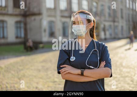 Junge Krankenschwester mit Gesichtsschutz und Maske für die Sicherheit, die erforderlich ist, um Covid19 zu verhindern, an einem sonnigen Tag im Freien zu stehen Stockfoto