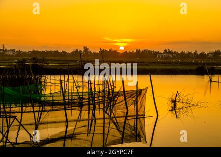 Das Wasser ist wie Glas, wenn die Sonne über den Ufern des Bon River mit einer runden Fischfangfalle in der Mitte untergeht. Stockfoto