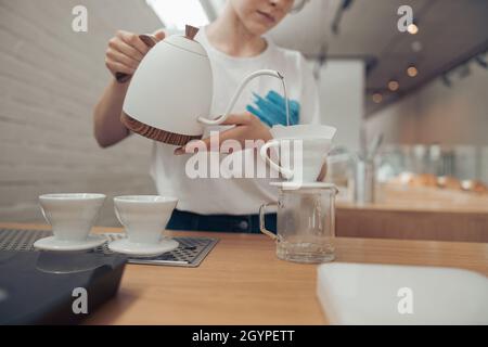 Barista gießt gekochtes Wasser durch den Filter in den Becher Stockfoto