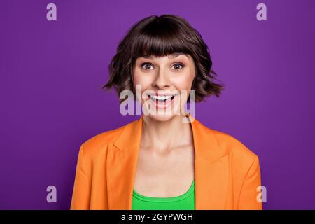 Foto von beeindruckt süße junge Frau gekleidet orange Blazer lächelnd isoliert lila Farbe Hintergrund Stockfoto