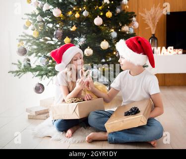 Kinder - ein Junge und ein Mädchen spielen in der Nähe des Weihnachtsbaums. Wohnzimmer mit Weihnachtsbaum und Dekorationen. Neujahr. Geschenk geben. Stockfoto