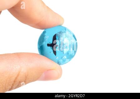 Nahaufnahme von weiblichen Fingern, die eine kleine blaue Kugel aus Glas mit Wolken und einem fliegenden Vogel im Inneren halten. Stockfoto