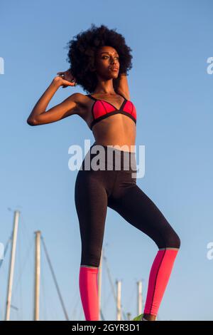 Junge athletische Frau in Sportkleidung, die sich mit einem blauen Himmel vor Hintergrund ausdehnt Stockfoto