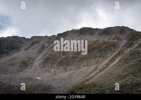 Beeindruckender, felsiger, abgelegener Bergrücken und Gipfel auf dem Rila-Berg, mit zwei weit entfernten Bergwanderern auf dem Gipfel Stockfoto
