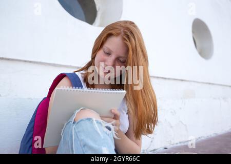 Das Teenager-Mädchen zeichnet das Skizzenbuch, während es auf den Stufen sitzt. Stockfoto