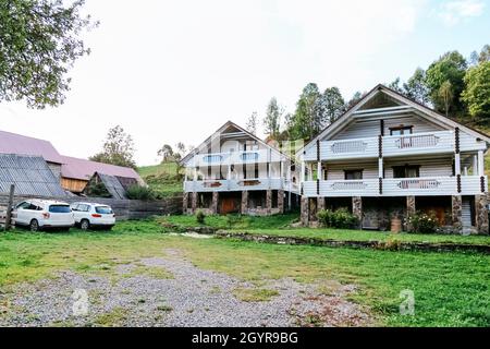 Zwei schöne weiße Holz-Chalet-Hütten Häuser und 2 weiße Autos in Bergdorf schöne ländliche Landschaft. Modernes Leben in der Natur außerhalb der Stadt Stockfoto