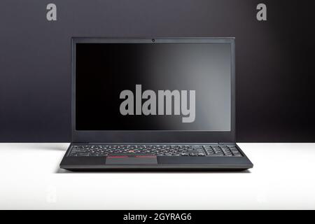 Leerer offener Laptop mit Mockup auf weißem Schreibtisch mit schwarzem Bildschirm. Minimalistischer Arbeitsbereich mit modernem Notebook. Bildschirmvorlage für persönliche Laptops für Stockfoto