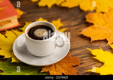Kaffeetasse auf Holztisch mit Buch bunten herbstlichen Ahornblättern. Stockfoto