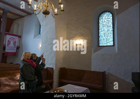 Sachsen Anhalt, Deutschland. Oktober 2021. 09. Oktober 2021, Sachsen-Anhalt, Altjeßnitz: In der kleinen romanischen Kirche im Landschaftspark Altjeßnitz sehen die Besucher eines der modernen Kirchenfenster, die der Künstler B. Muhr entworfen hat. Diese neuen Fenster sind Teil des Projekts „Lichtungen“ der Evangelischen Landeskirche Anhalt, das zeitgenössische Glasmalerei in historische Kirchen Anhalts bringt. Die Fenster wurden bereits im vergangenen Jahr mit Unterstützung der Landeskirche Anhalt und der Ecclesia Foundation installiert, konnten aber aufgrund der Corona-Pandemie bis jetzt nicht eingeweiht werden. Foto: Hei Stockfoto