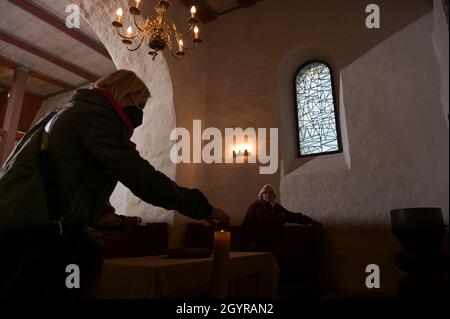 Sachsen Anhalt, Deutschland. Oktober 2021. 09. Oktober 2021, Sachsen-Anhalt, Altjeßnitz: Zur Einweihung der neuen Kirchenfenster des Künstlers B. Muhr zündet ein Besucher in der kleinen romanischen Kirche im Landschaftspark Altjeßnitz eine Kerze an. Diese neuen Fenster sind Teil des Projekts „Lichtungen“ der Evangelischen Landeskirche Anhalt, das zeitgenössische Glasmalerei in die historischen Kirchen Anhalts bringt. Die Fenster wurden bereits im vergangenen Jahr mit Unterstützung der Landeskirche Anhalt und der Ecclesia Foundation installiert, konnten aber aufgrund der Corona-Pandemie bis jetzt nicht eingeweiht werden. Ph Stockfoto