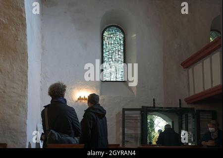 Sachsen Anhalt, Deutschland. Oktober 2021. 09. Oktober 2021, Sachsen-Anhalt, Altjeßnitz: In der kleinen romanischen Kirche im Landschaftspark Altjeßnitz sehen die Besucher eines der modernen Kirchenfenster, die der Künstler B. Muhr entworfen hat. Diese neuen Fenster sind Teil des Projekts „Lichtungen“ der Evangelischen Landeskirche Anhalt, das zeitgenössische Glasmalerei in historische Kirchen Anhalts bringt. Die Fenster wurden bereits im vergangenen Jahr mit Unterstützung der Landeskirche Anhalt und der Ecclesia Foundation installiert, konnten aber aufgrund der Corona-Pandemie bis jetzt nicht eingeweiht werden. Foto: Hei Stockfoto