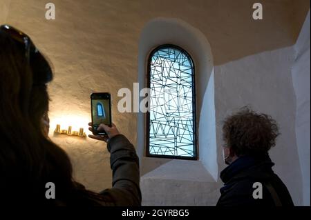 Sachsen Anhalt, Deutschland. Oktober 2021. 09. Oktober 2021, Sachsen-Anhalt, Altjeßnitz: Ein Besucher fotografiert eines der modernen Kirchenfenster, die der Künstler B. Muhr in der kleinen romanischen Kirche im Landschaftspark Altjeßnitz entworfen hat. Diese neuen Fenster sind Teil des Projekts „Lichtungen“ der Evangelischen Kirche Anhalt, das zeitgenössische Glasmalerei in historische Kirchen Anhalts bringt. Die Fenster wurden bereits im vergangenen Jahr mit Unterstützung der Landeskirche Anhalt und der Ecclesia Foundation installiert, konnten aber aufgrund der Corona-Pandemie bis jetzt nicht eingeweiht werden. Foto: He Stockfoto