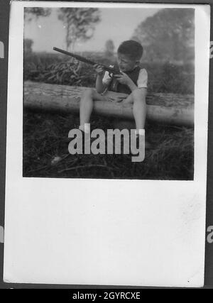 Kleiner Junge in Shorts, der mit einem Gewehr spielt Stockfoto