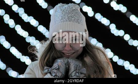 Das Mädchen friert abends im Winter in der Stadt vor dem Hintergrund von Gerlands ein. Stockfoto