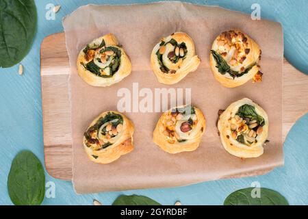 Blätterteig mit Spinat und Feta-Käse, zu Spiralen aufgerollt, frisch aus dem Ofen, blauer Hintergrund Stockfoto